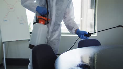 sección media del trabajador de la salud con ropa de protección limpiando la oficina usando spray desinfectante