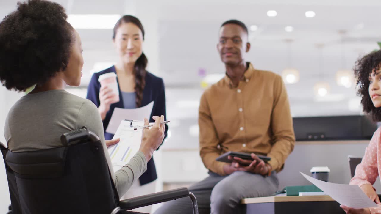 Group of diverse and disabled business people holding documents and talking in office, slow motion