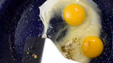 two eggs cooking in frying pan with added pepper top view