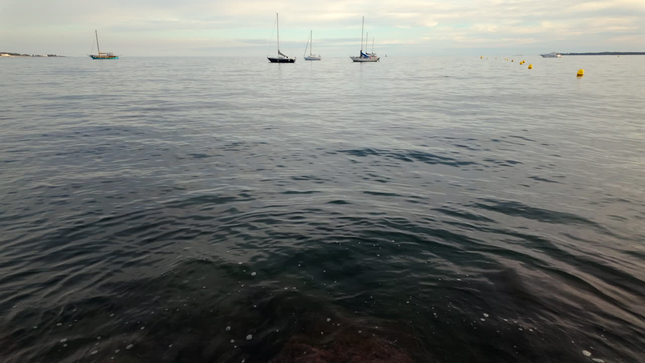 Several sailboats floating peacefully on calm water under a cloudy sky