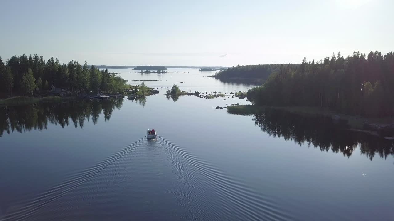 моторная лодка медленно движется между островами, спокойное море в тихом северном архипелаге в солнечный летний день, съемка с беспилотного летательного аппарата, снижающегося и наклоняющегося вверх