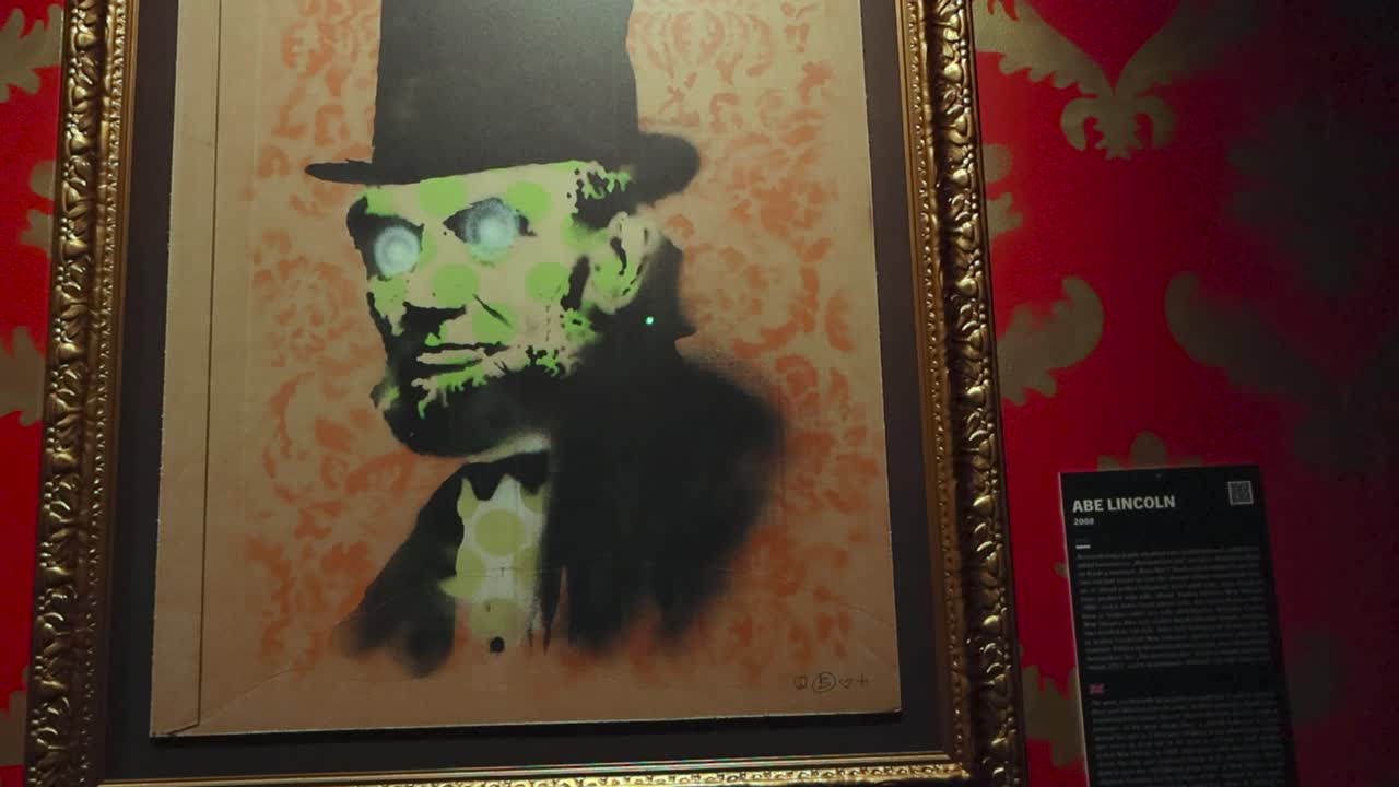 Painting called Abe Lincoln done by Banksy on display at his art exhibition. Done in multilayered stencil art style the president has a tall top hat on and his face is covered in green dots.
