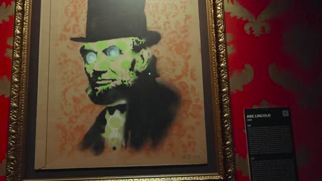 painting called abe lincoln done by banksy on display at his art exhibition. done in multilayered stencil art style the president has a tall top hat on and his face is covered in green dots.