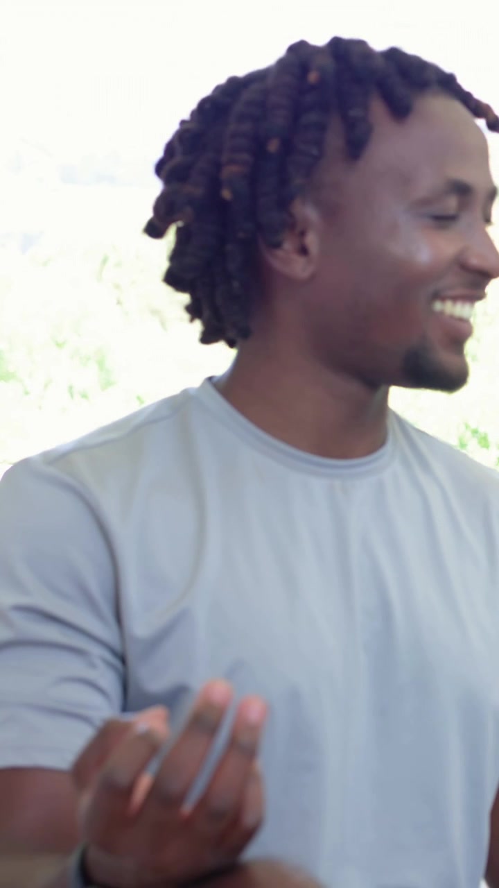 Vertical video: Meditating man turning head opening eyes laughing on porch light grey tee open palm