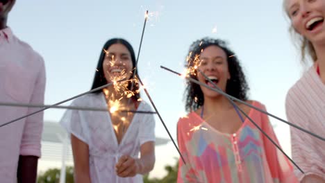 un grupo feliz y diverso de amigos quemando chispas en círculo en la playa