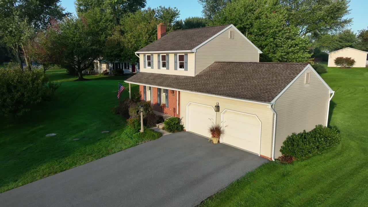 Two-story home with attached garage, American flag, and lush trees in a suburban area.