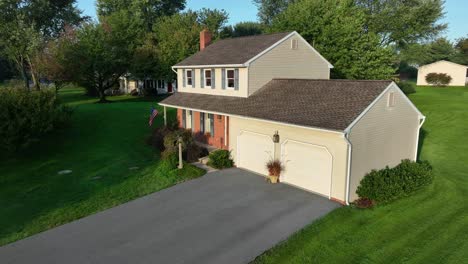two-story home with attached garage, american flag, and lush trees in a suburban area.