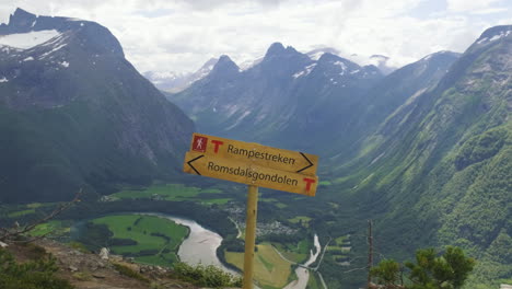Yellow-Road-Signage-At-The-Clifftop-With-A-View-Of-A-River-And-Mountain-Range-In-Andalsnes,-Norway