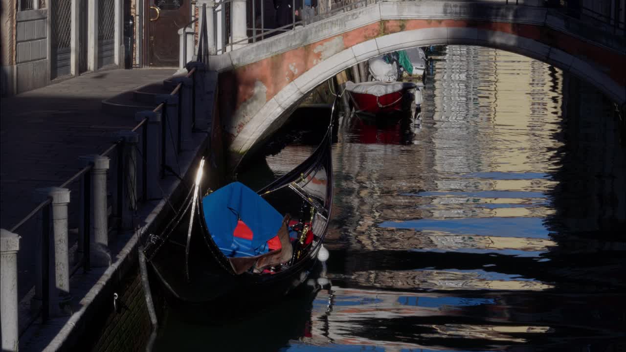Gondola ormeggiata in un canale soleggiato di Venezia sotto un ponte ad arco