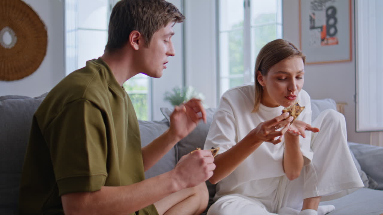 Hungry friends enjoying pizza watching TV at home sofa closeup. Happy people