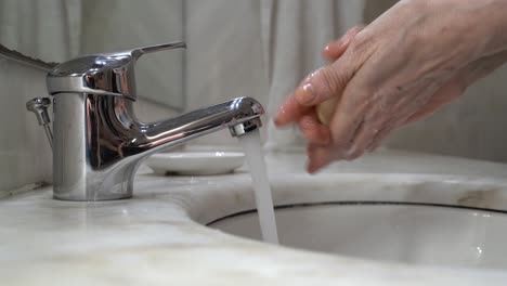 old woman's hand's are washed on tap water with soap, then rinsed and wiped on a white cloth towel - top view static medium shot