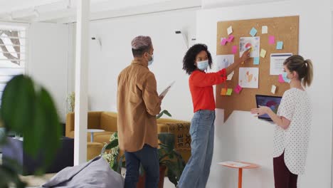 Woman-wearing-face-mask-discussing-over-memo-notes-with-her-colleagues-at-office