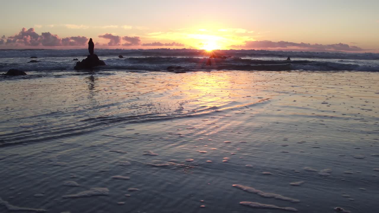 Vista mozzafiato del tramonto con la bassa marea a Laguna Beach, mentre il sole spunta tra le rocce e si riflette sull'acqua.
