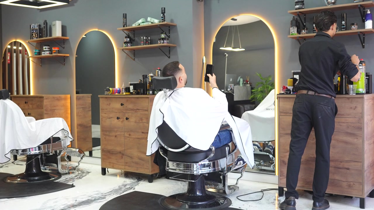 Giovane uomo seduto su una poltrona da barbiere professionale mentre si fa tagliare i capelli da uno stilista.
