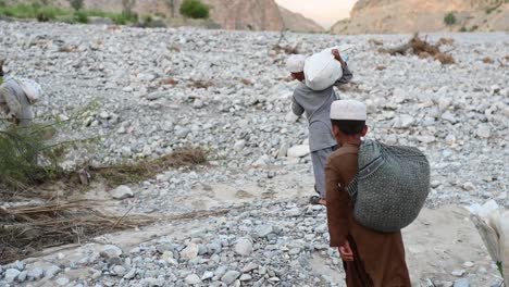 video of the two small children and a man carrying heavy sacks on their shoulder and walking in the broken road in baloschistan