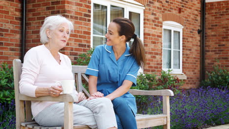 Senior-Woman-Sitting-On-Bench-And-Talking-With-Nurse-In-Retirement-Home