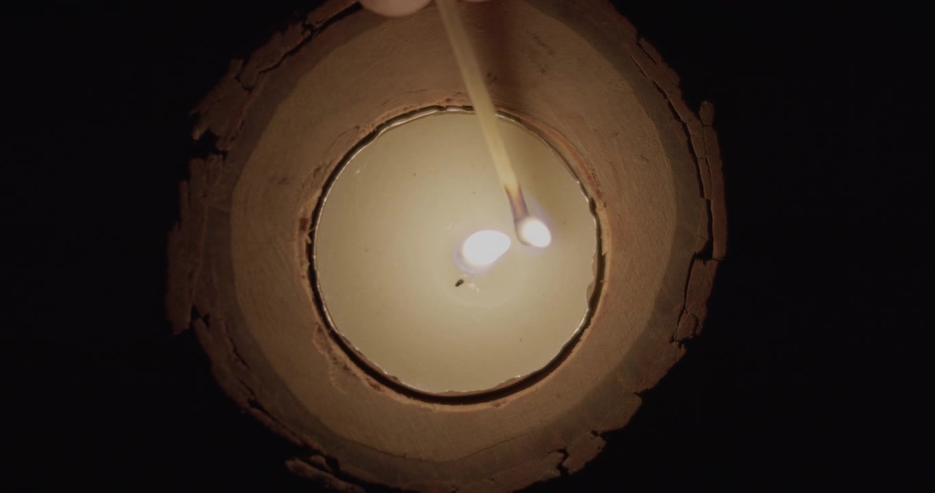 Mano che accende una candela con un fiammifero