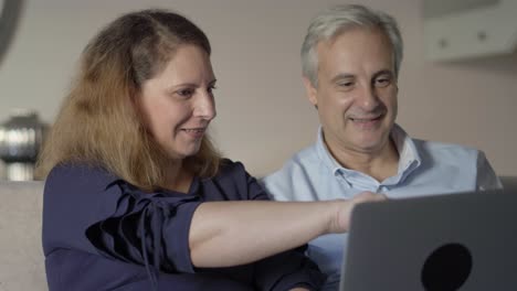 pareja adulta positiva con computadora portátil discutiendo una nueva aplicación en línea