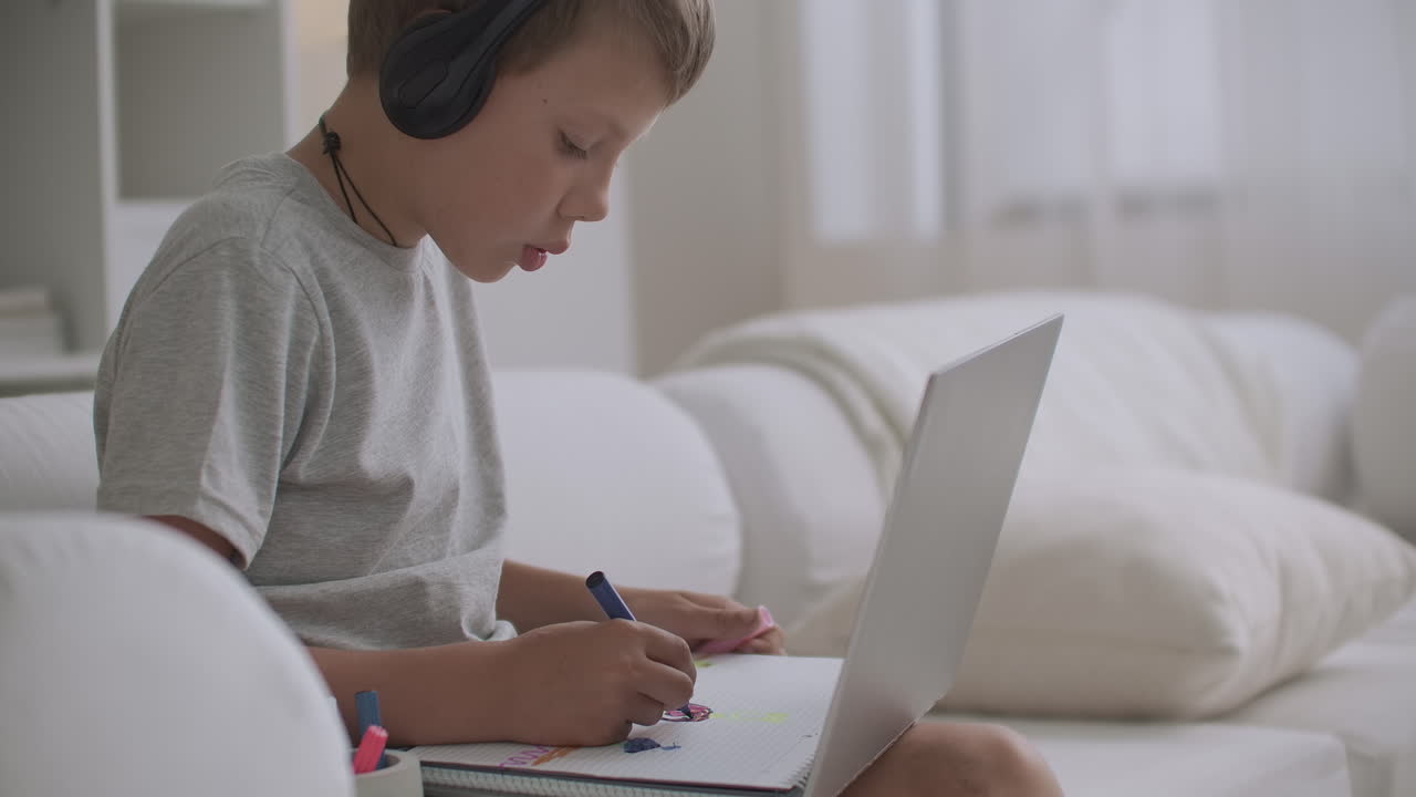 retrato de un niño con auriculares en la cabeza dibujando niño está sentado en la mesa en su habitación