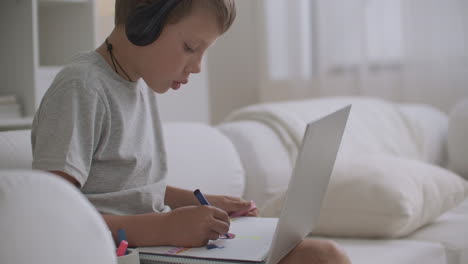 Porträt-Eines-Kleinen-Jungen-Mit-Kopfhörern-Auf-Dem-Kopf,-Der-Ein-Kind-Zeichnet,-Das-Am-Tisch-In-Seinem-Zimmer-Sitzt