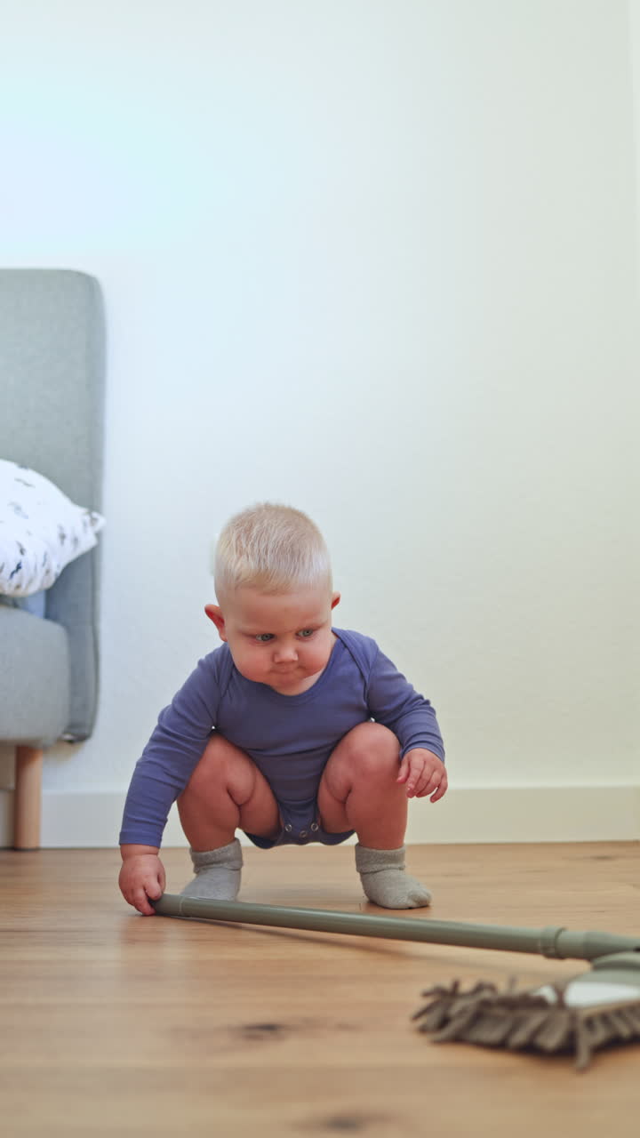 Un bambino piccolo lava il pavimento con un mop. Il bambino aiuta a pulire il pavimento. Un bambino in un body di cotone