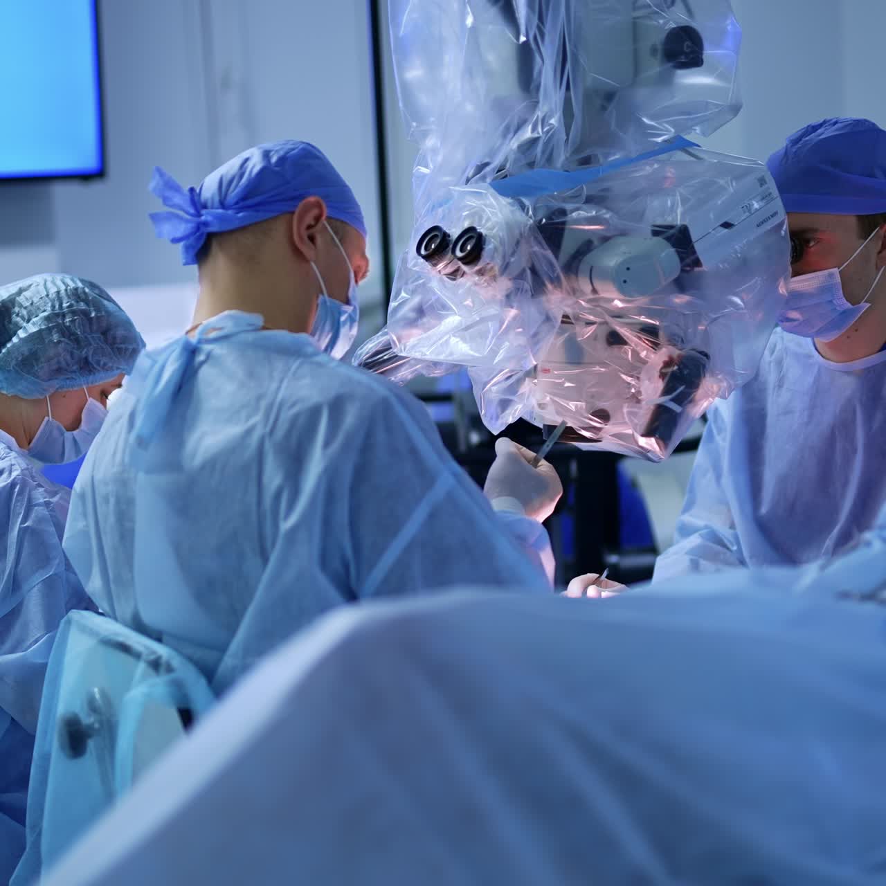 Neurosurgeons collaborate at neurosurgical operation. Doctor looks at modern microscope covered in plastic. Female nurse assisting