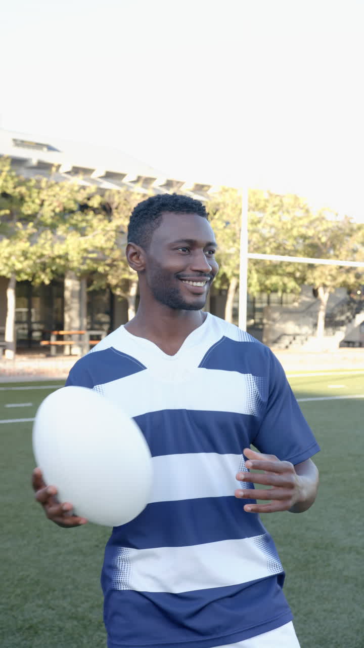 Video vertical: Atleta sonriendo sosteniendo un balón de rugby en el campo, disfrutando de una sesión de práctica al aire libre.