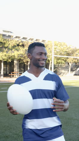 vertical video: smiling athlete holding rugby ball on field, enjoying outdoor practice session