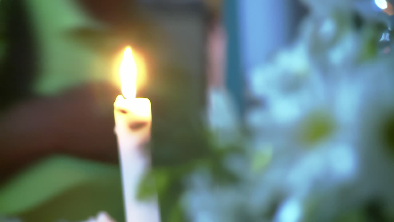 Una candela brucia mentre la telecamera sposta la messa a fuoco sui fiori in primo piano