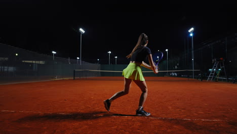 woman playing tennis at night on clay court