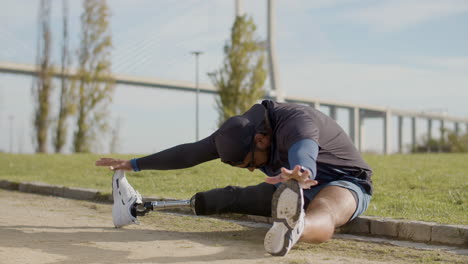 sportsman with artificial leg sitting and stretching legs outdoors