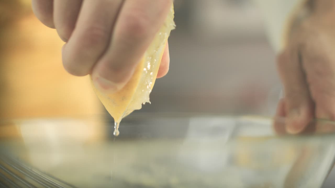Close up of a lemon being squeezed until lemon juice drops fall into a glass bowl by a vegan chef