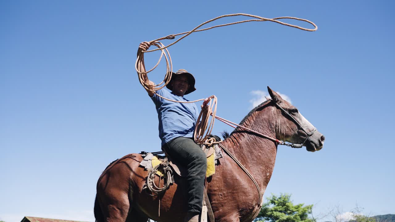 Cowboy a cavallo con lazo contro il cielo blu