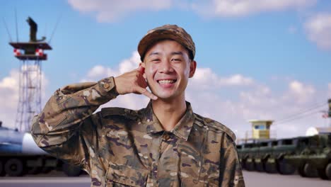 위장 유니폼을 입은 미소 짓는 군인이 전화 제스처를 하고 있습니다.