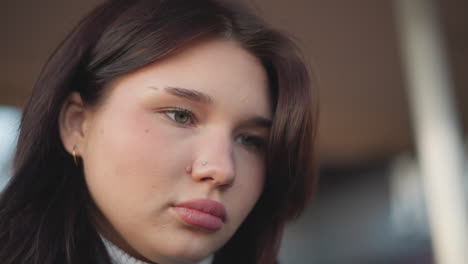 close-up of woman with pink lips focusing on something in front of her, showcasing her natural beauty, with a subtle nose ring and soft, focused expression in a blurred background