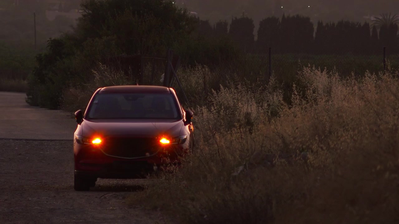 Auto rossa con luci di emergenza lampeggianti su una strada di campagna al tramonto