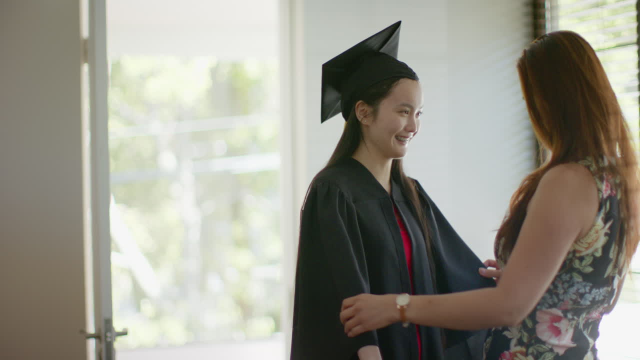Graduating, young woman in cap and gown holding hands with asian mother
