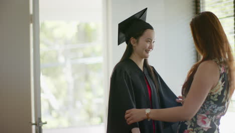graduating, young woman in cap and gown holding hands with asian mother