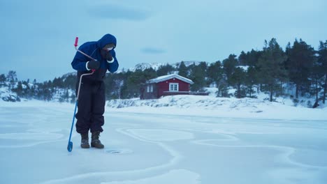 un hombre está usando un perforador de hielo manual para perforar un agujero para la pesca en hielo en bessaker, condado de trondelag, noruega - toma estática