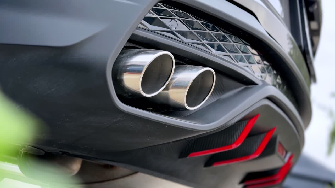 Modern bir performans aracının çift krom egzoz borularının ve arka tampon detaylarının gün ışığında dış mekanda yakın çekimi, sportif otomotiv tasarımını ve agresif stilini vurguluyor