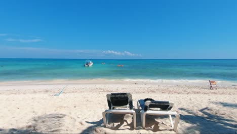 Gorgeous-tilting-up-shot-of-a-tropical-beach-with-tourists-swimming-and-a-small-boat-next-to-them-on-the-beautiful-Playa-del-Carmen-in-Riviera-Maya,-Mexico-near-Cancun-on-a-summer-day-on-vacation