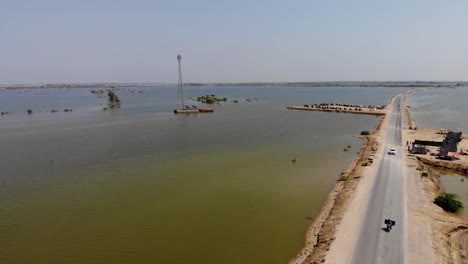 Vista-Aérea-Del-Paisaje-De-Jacobabad-Bajo-El-Agua-De-La-Inundación-Con-Un-Camino-Que-Atraviesa