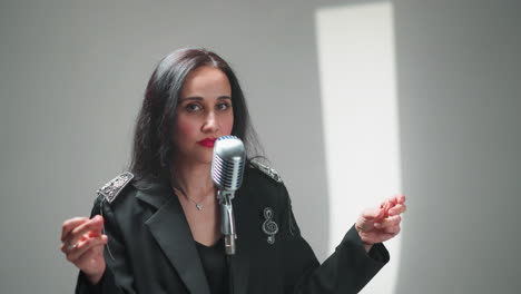 woman in a black outfit snapping fingers in front of a vintage microphone, set against a white background with studio lighting and a red keyboard in the background