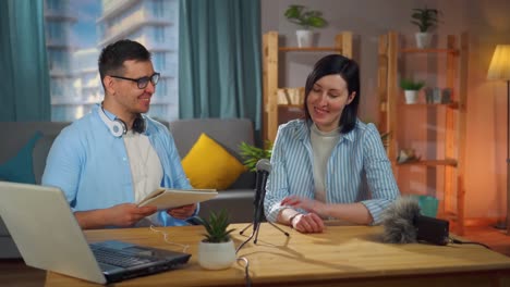 man with glasses and a woman sitting in a home recording studio recording a podcast interview