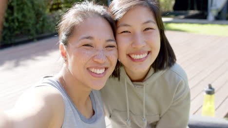 Happy-asian-female-friends-with-water-bottle-doing-selfie-and-laughing-on-terrace,-slow-motion