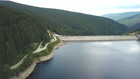 forward drone shot over a lake towards a dam on a cloudy day with a forest in the background