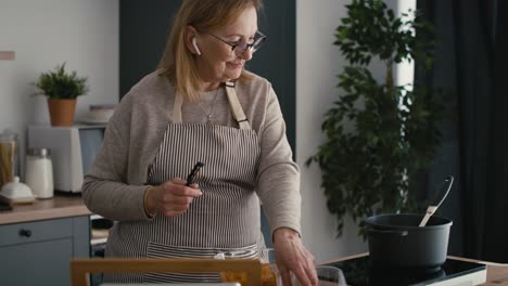 Kaukasische-ältere-Frau,-Die-über-Kopfhörer-Kocht-Und-Chattet