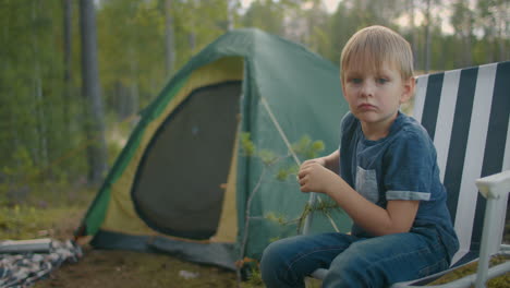 Retrato-De-Un-Niño-Pequeño-En-Un-Campamento-Forestal,-Un-Niño-Está-Sentado-En-Una-Silla-Cerca-De-Una-Tienda-Turística-Y-Descansa-En-La-Naturaleza-En-Verano-U-Otoño