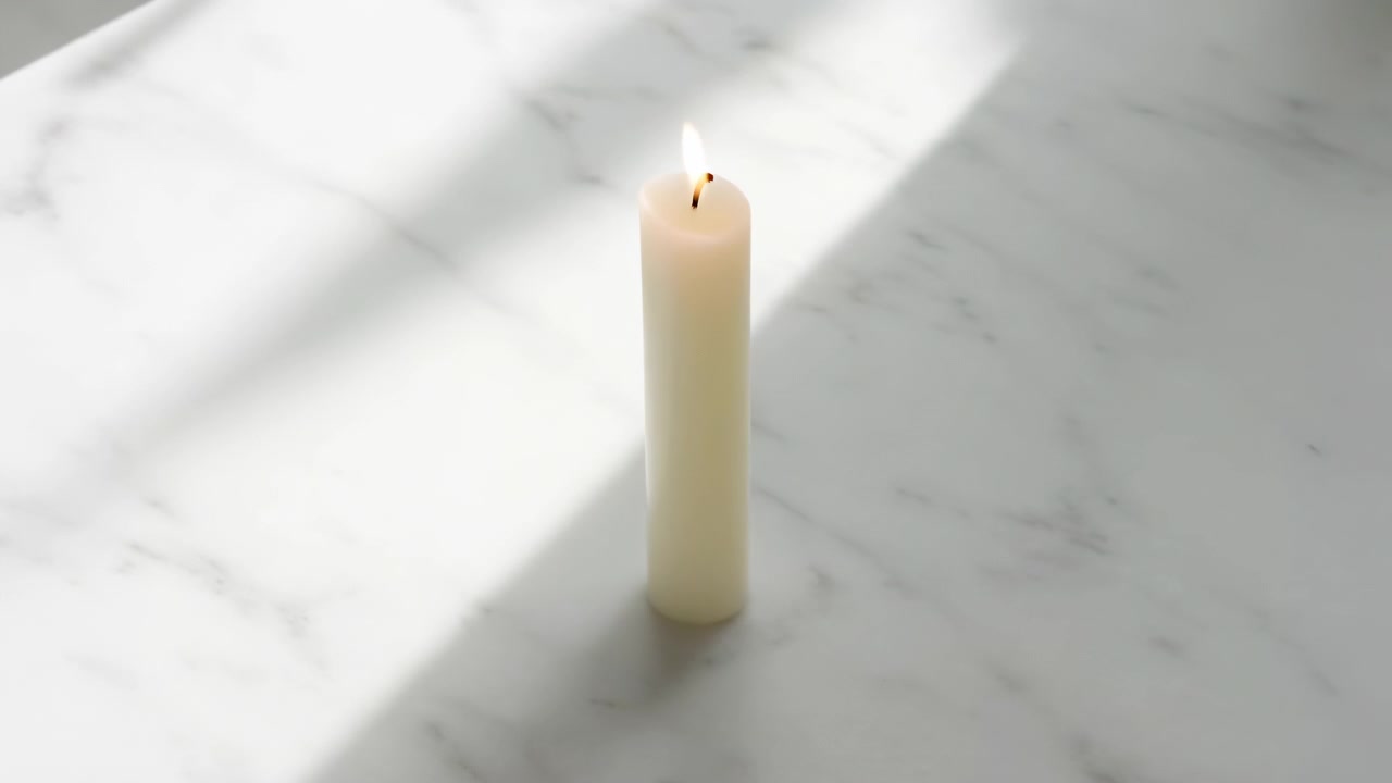 Ett enda krämfärgat ljus brinner på en blek marmoryta, med mjukt diagonalt solljus och en mild skugga som skapar en lugn minimalistisk inomhusscen.