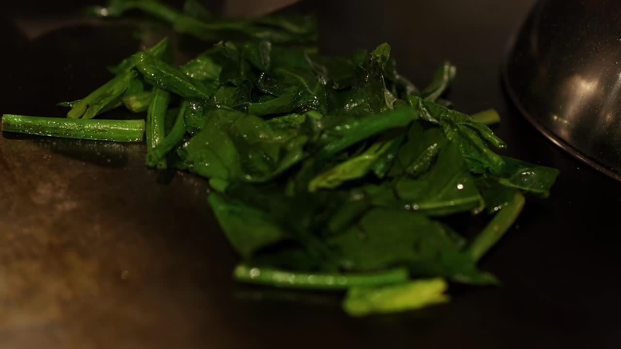 Detailed view of fresh spinach leaves being stirred with a spatula in a hot pan.
